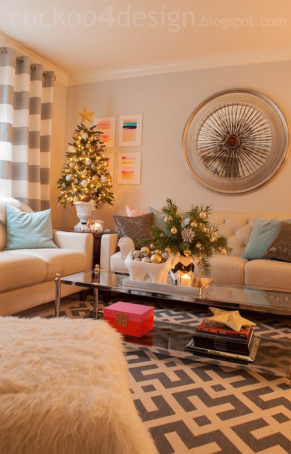 living room view with striped curtains, gray patterned rug, colorful thro pillows, pink and orange box, colorful abstract art and tabletop Christmas tree