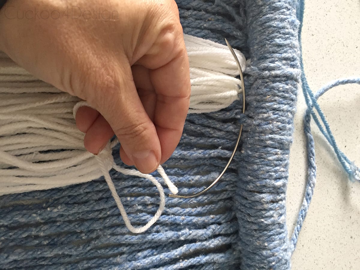 using a curved needle to attach wool to mop head yarn wall hanging