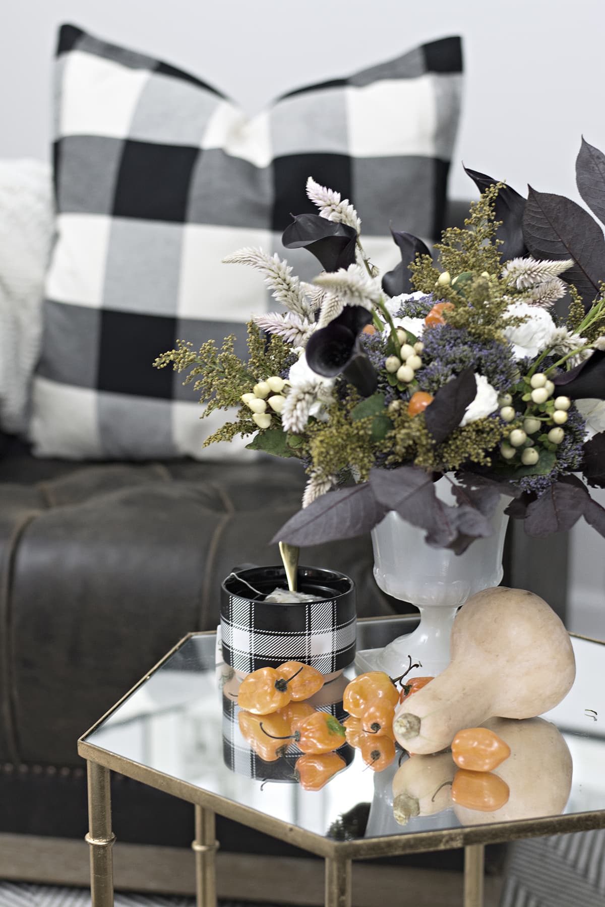 flower arrangement with black calla Lillies, orange hot peppers, in addition to the white grasses, white Hypericum Berries, golden rod, and purple flowers on coffee table