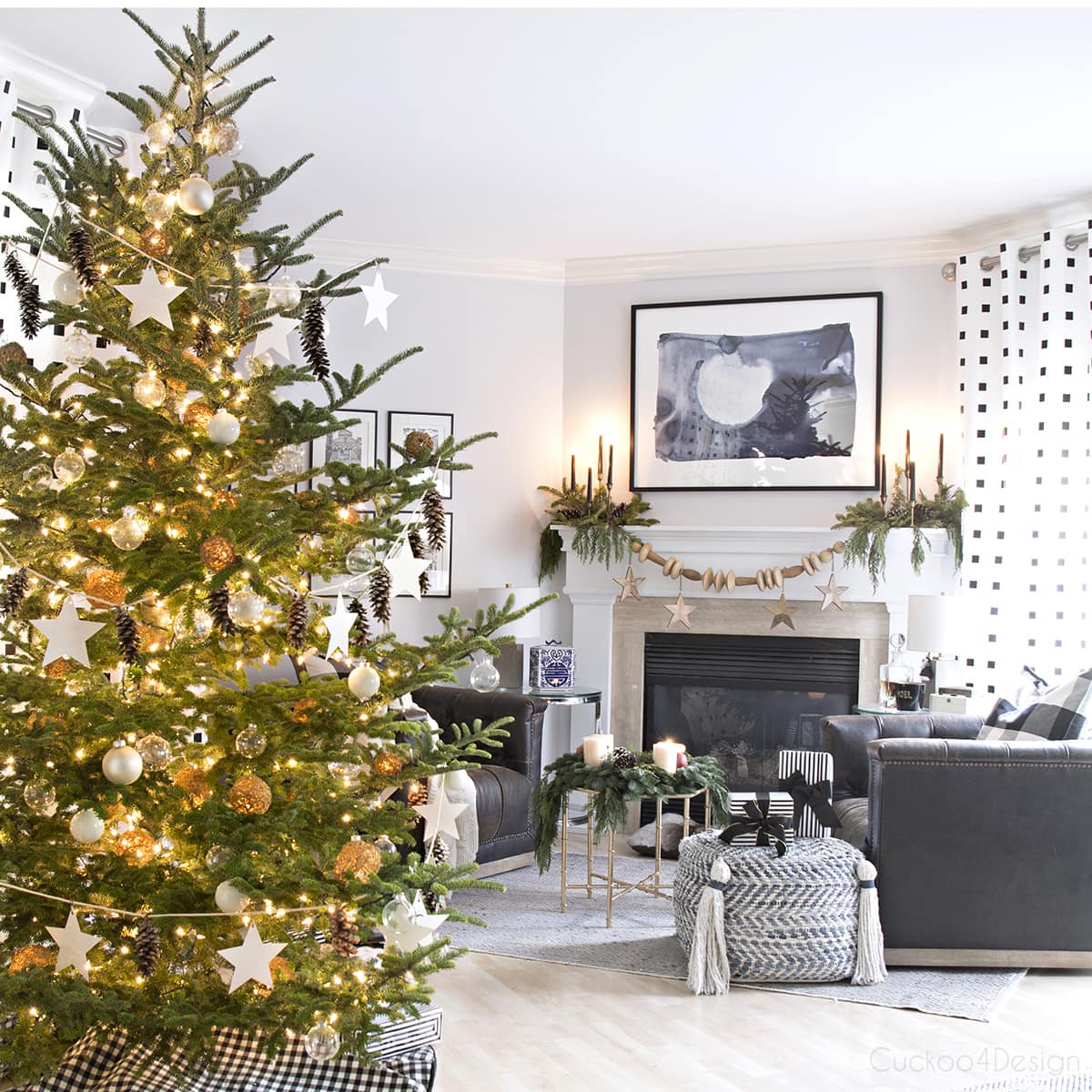 Modern European Eclectic Christmas Tree with pinecones, white stars, clear Christmas balls and white Christmas balls on a real untrimmed fir tree | blue, white and black fireplace area with leather swivel chairs