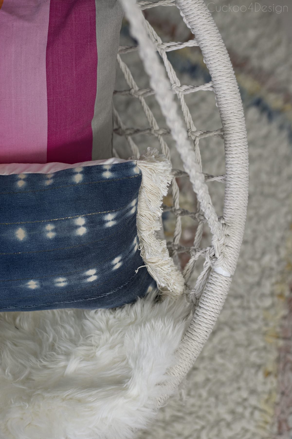 pretty hanging macrame chair in girls bedroom with dark blue walls, rainbow pillow and shibori fringe pillow