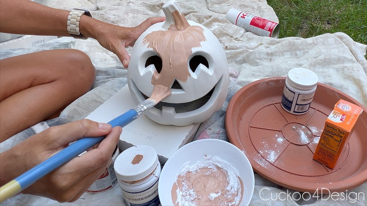 painting the first layer of faux terracotta baking soda paint onto plastic pumpkin