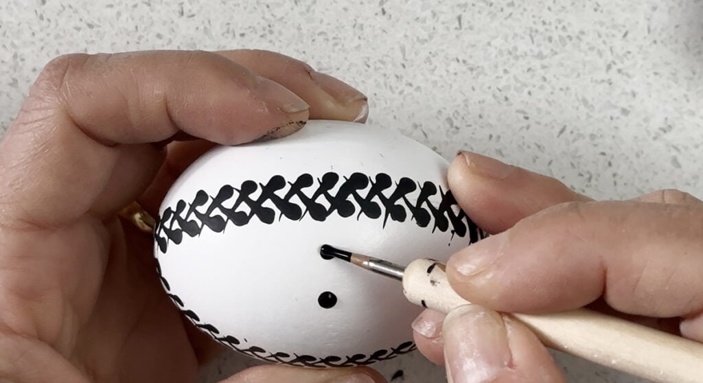 practicing pysanky egg designs on a white egg with black paint