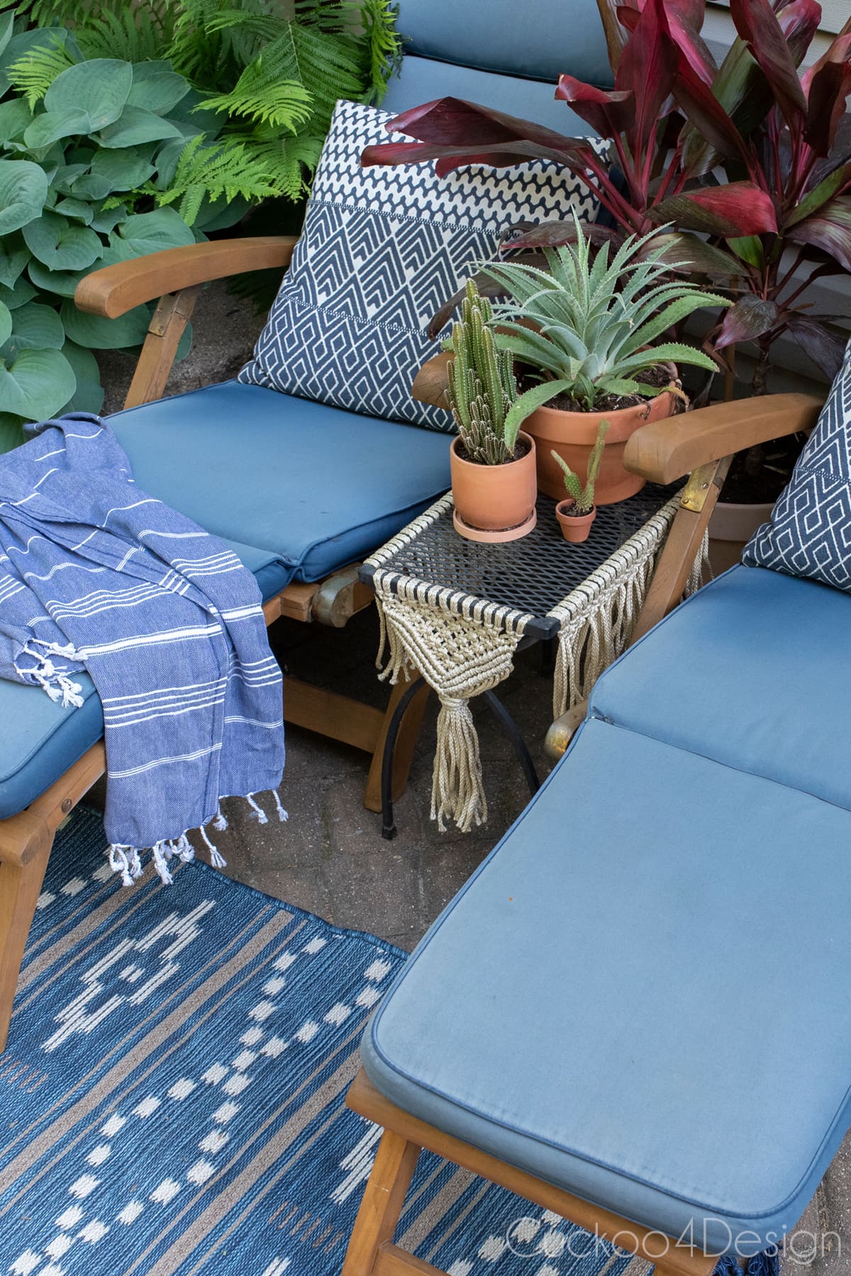 metal mesh patio table with macrame between two sun lounge chairs with blue accents and a lot of plants in terracotta pots
