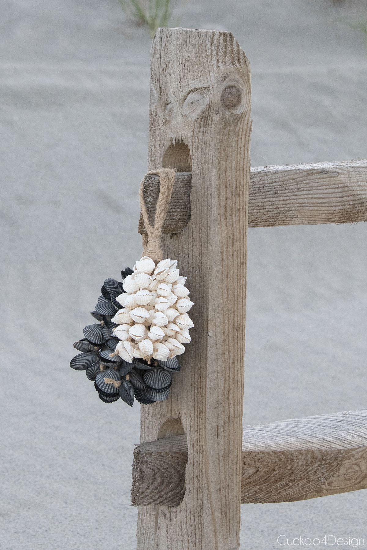 white seashell tassel and black scallop seashell tassel hanging on beach fence