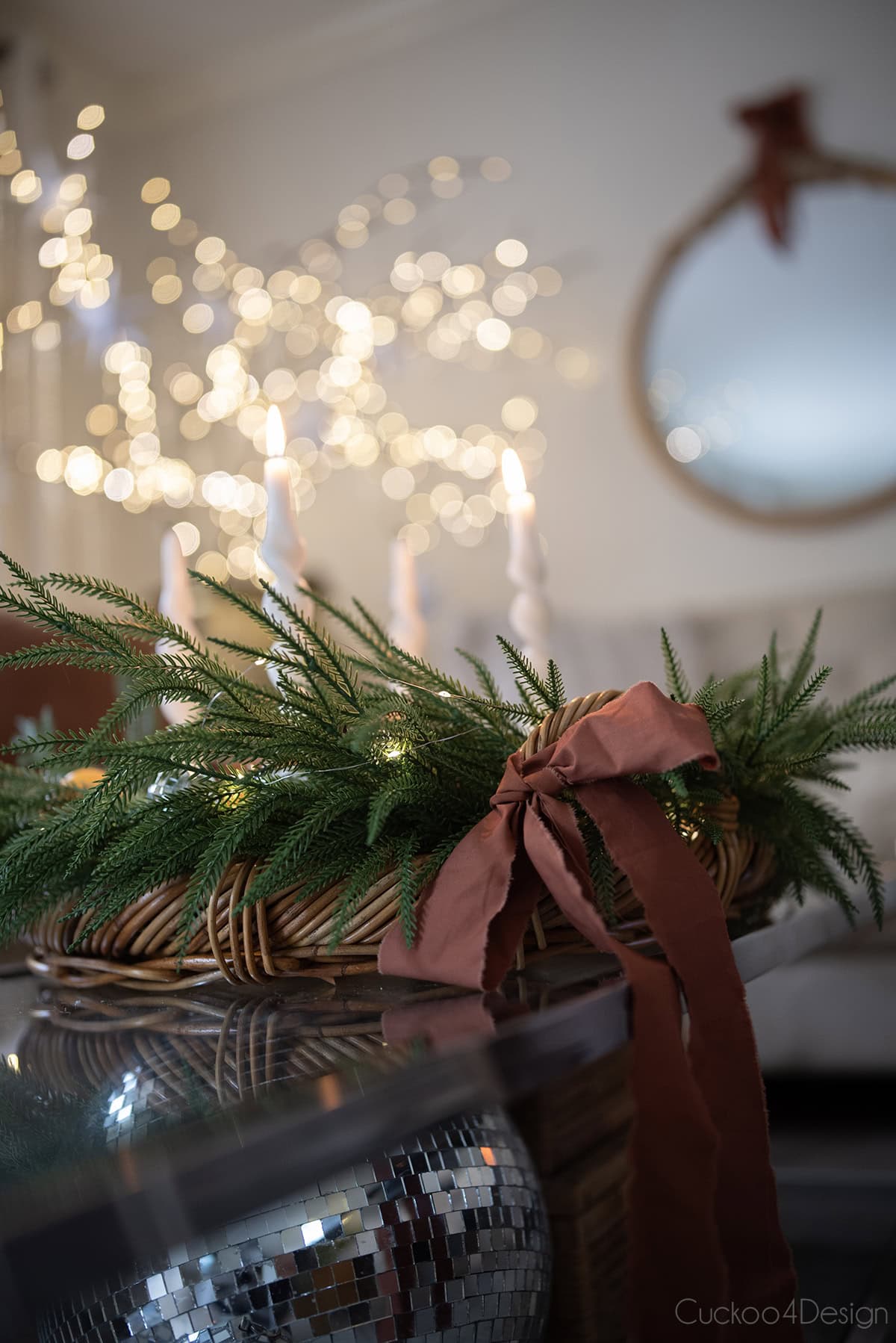 close-up of coffee table decorated with vintage basket tray, spiral candles, faux cedar garland, pinecones, fairy lights, advent candles, and disco balls