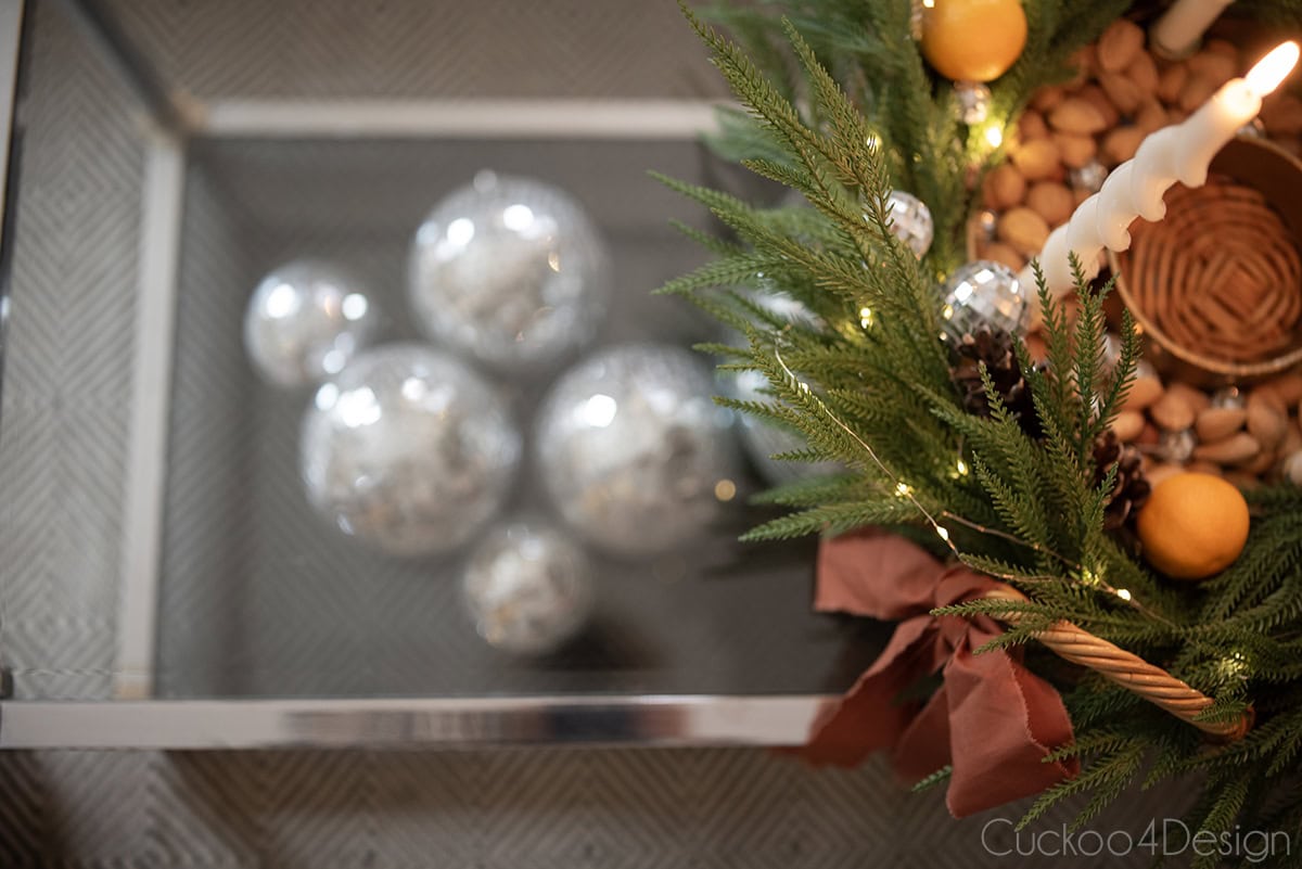 top view of coffee table decorated with vintage basket tray, faux cedar garland, pinecones, fairy lights, advent candles, and disco balls