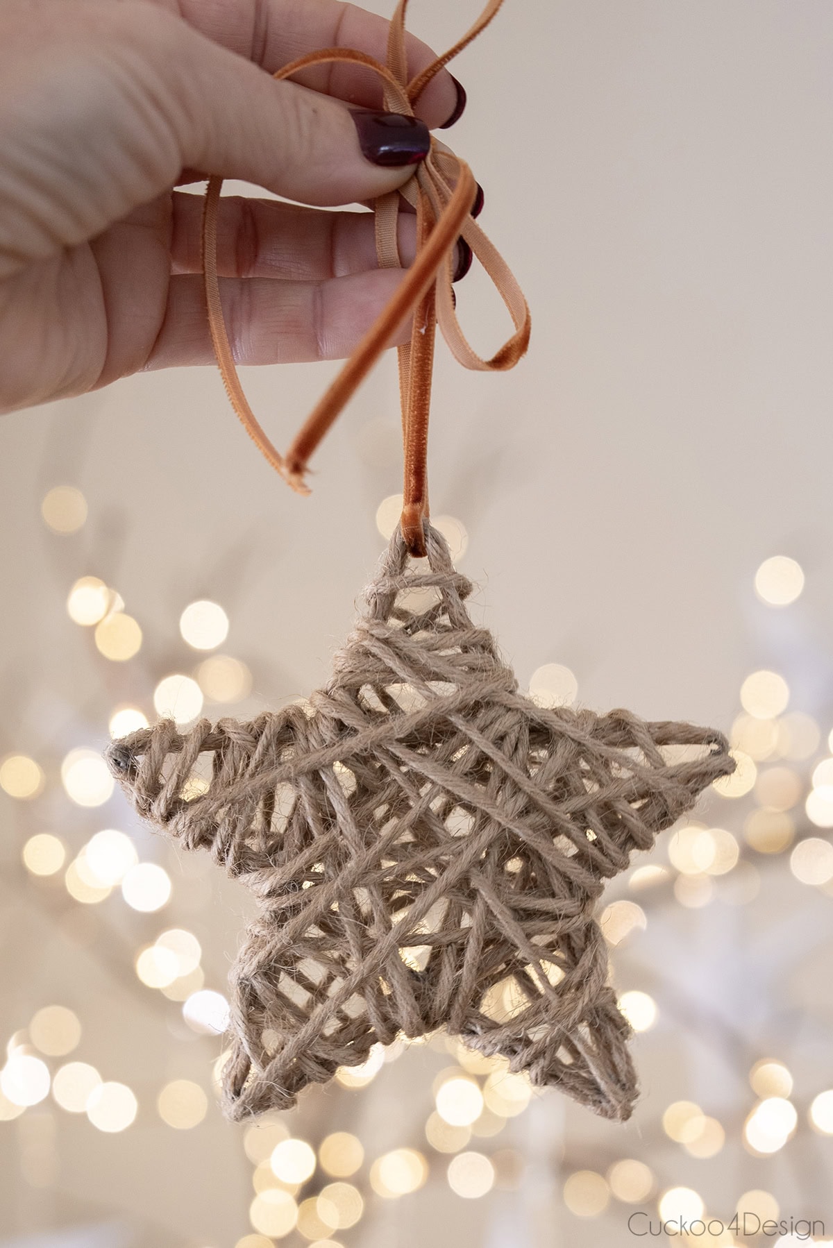 hand holding yarn star ornament with velvet ribbon in front of sparking lights