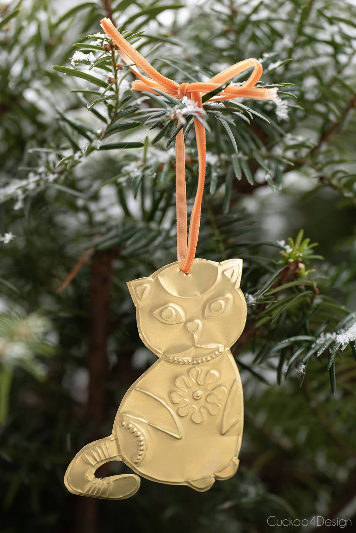 close-up of embossed tin cat ornament hanging in snowy pine tree