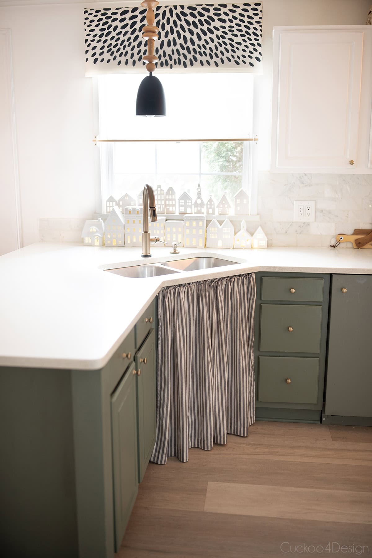 green kitchen cabinets with sink curtains and rows of white ceramic house window display as winter decor