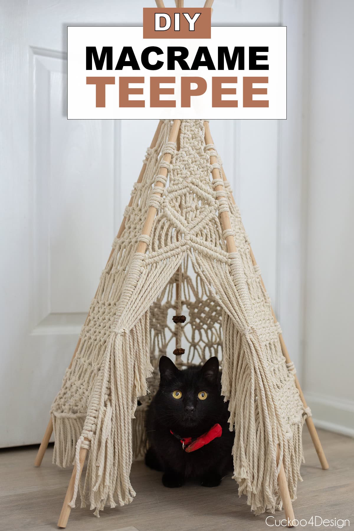 DIY macrame teepee with a black cat sitting in the opening against a white wall