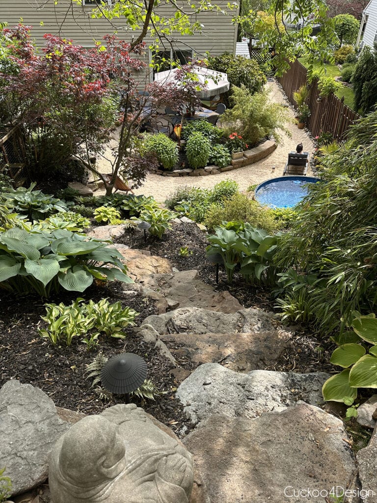 view from the top of the yard down onto the landscaped hill, stock tank pool, paver patio, and pea gravel areas