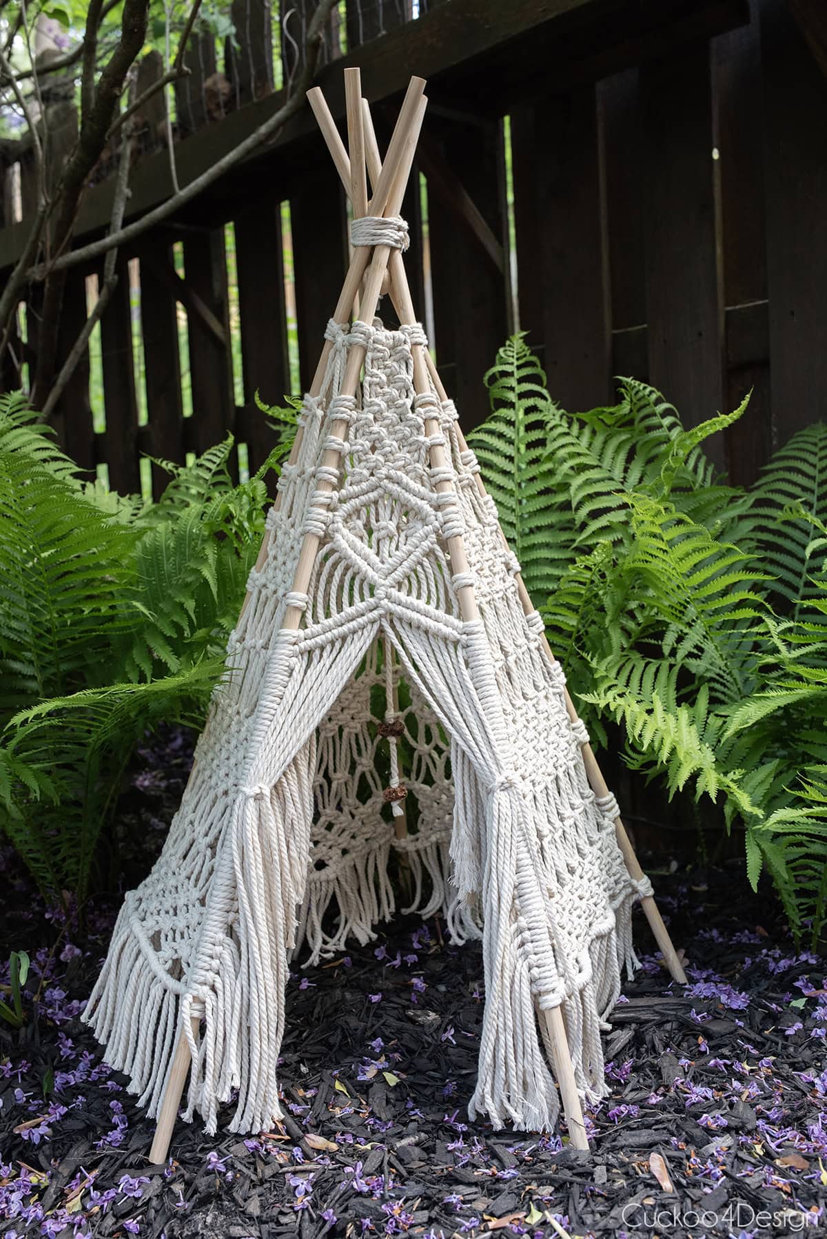 macrame teepee sitting in a flower bed surrounded by green ferns