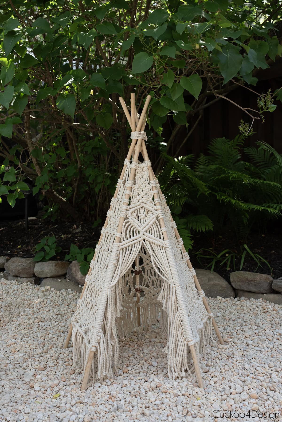 macrame teepee on pea gravel with dark green plants int the background