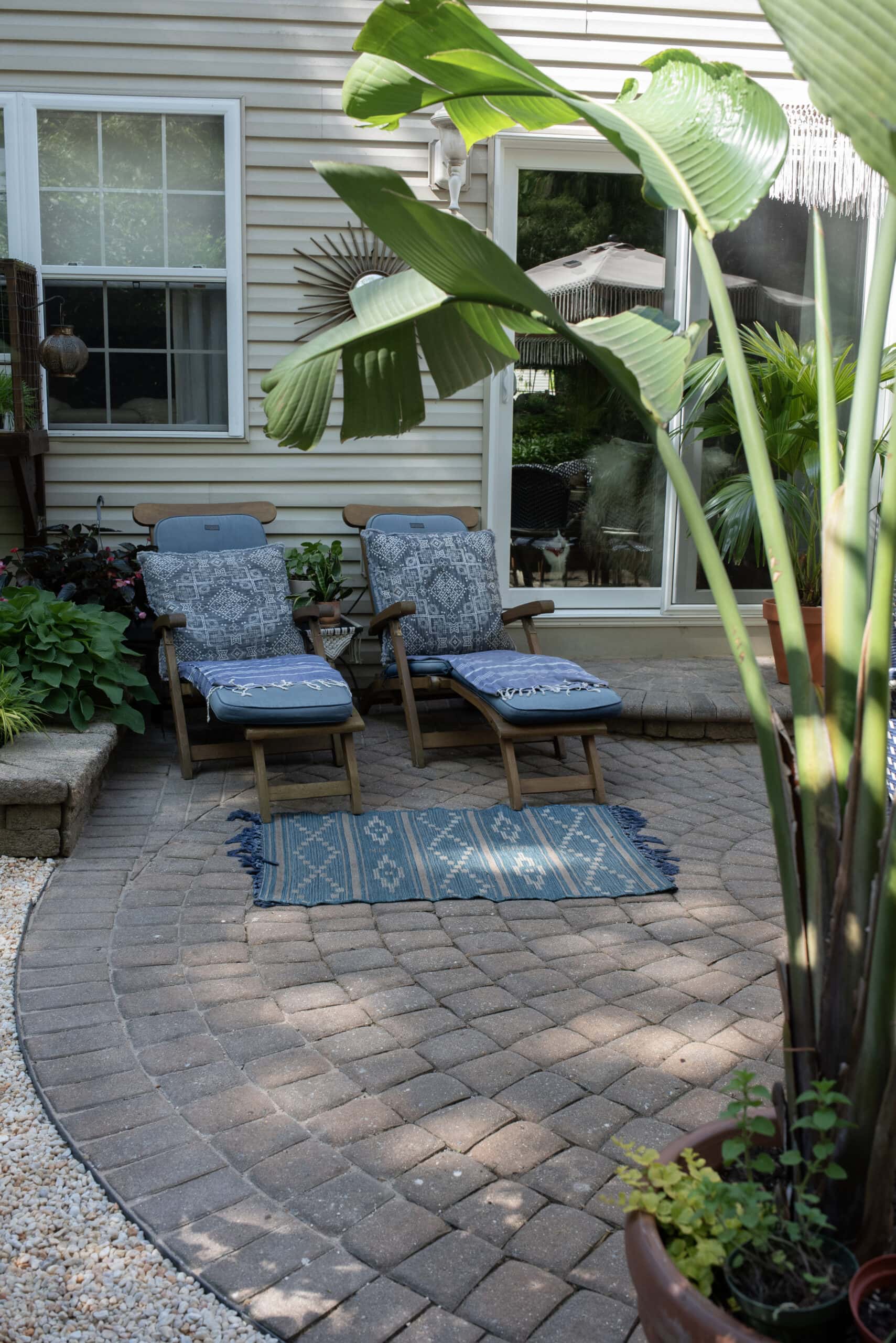 two teak lounge chairs on paver patio with plants