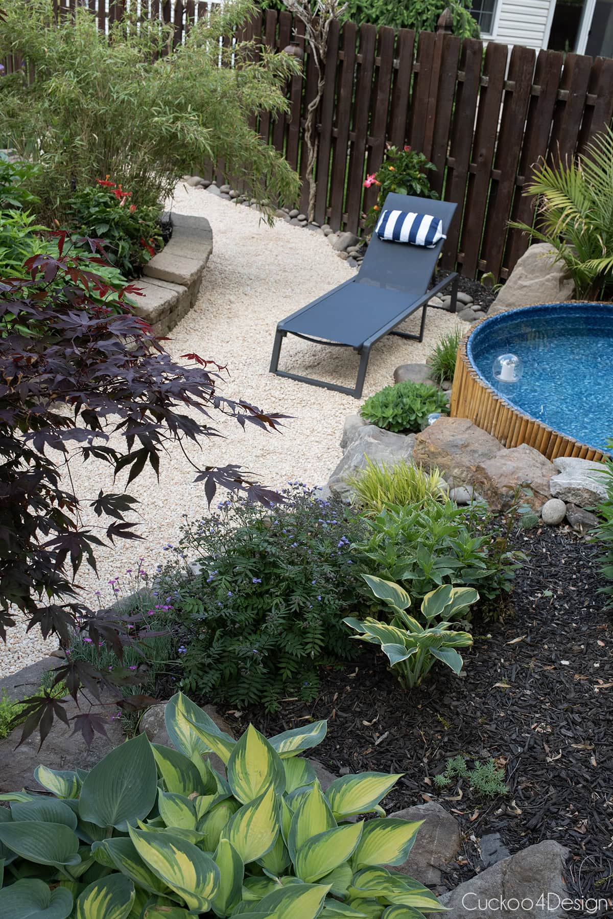 view from above the flower beds into the garden with pea gravel, lounge chair and stock tank pool