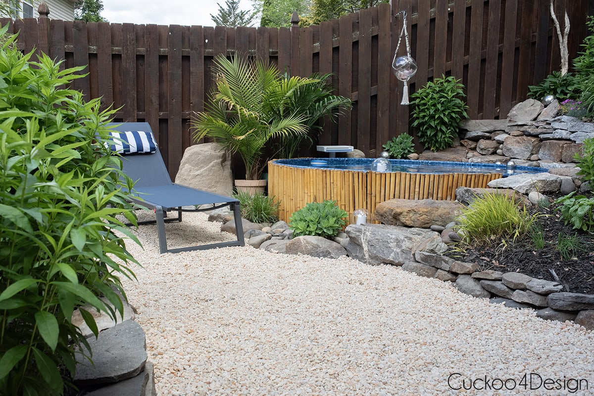 full view of stock tank pool with lounge chair on pea gravel and plants