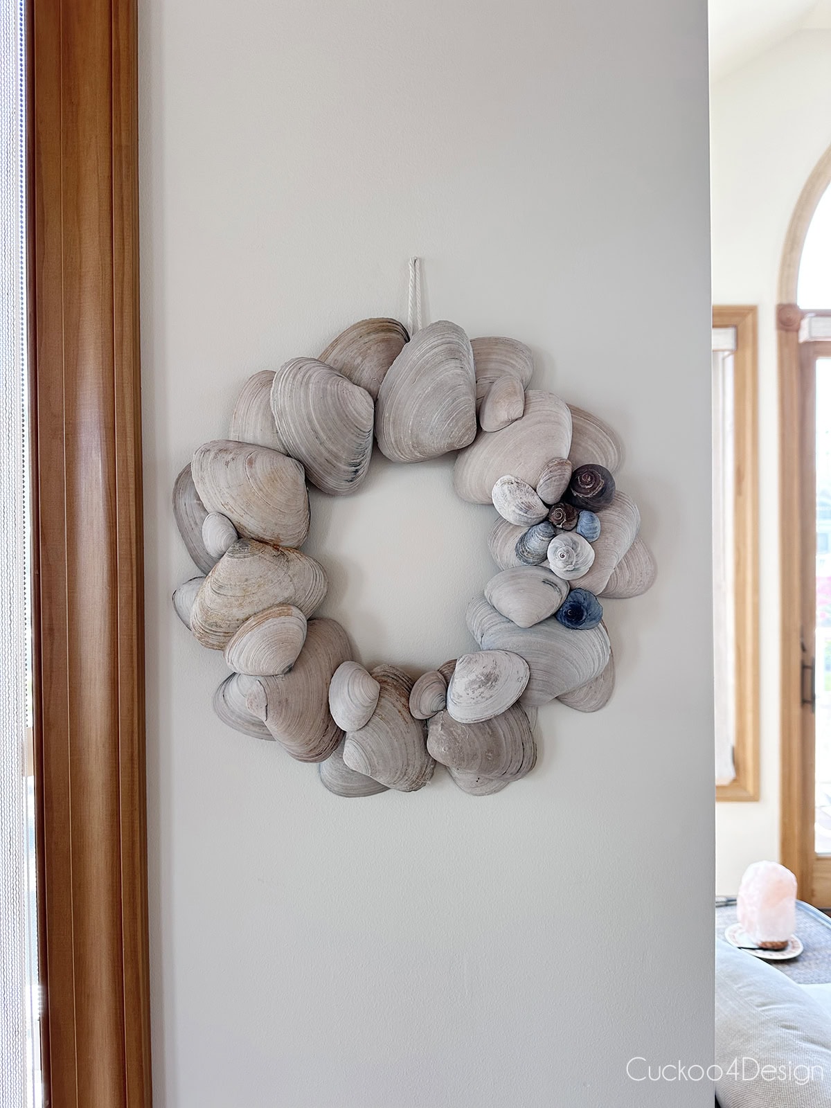 DIY seashell wreath made with large clam shells and with snail shell detail hanging on a beach house wall