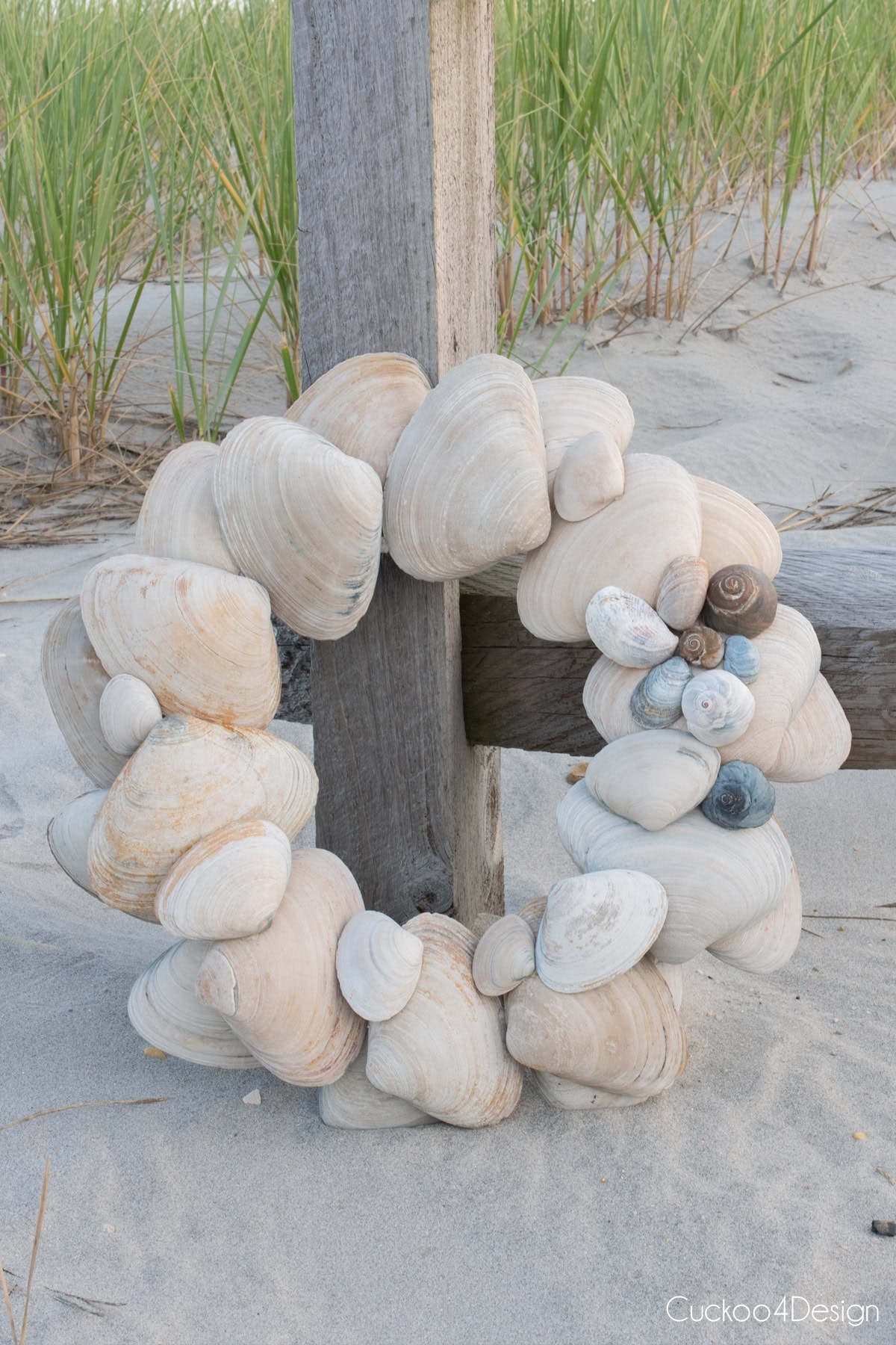 DIY seashell wreath made with large clam shells and with snail shell detail leaning on dune fence