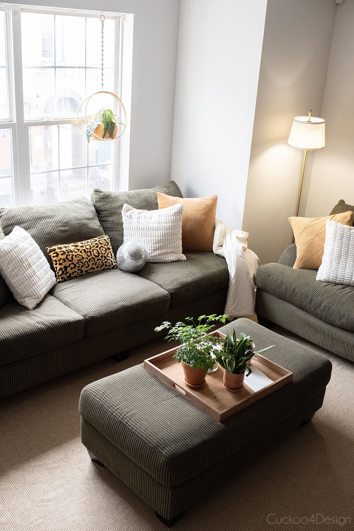floor lamp lit next to army green corduroy sofa with leopard accents