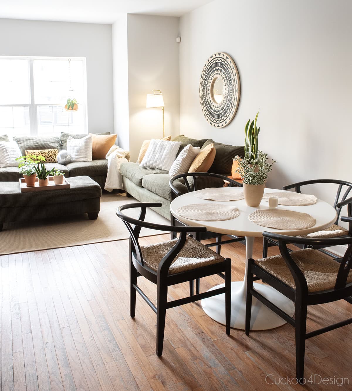view from college apartment dining room with white pedestal table and wishbone chairs into the living room with army green sofa