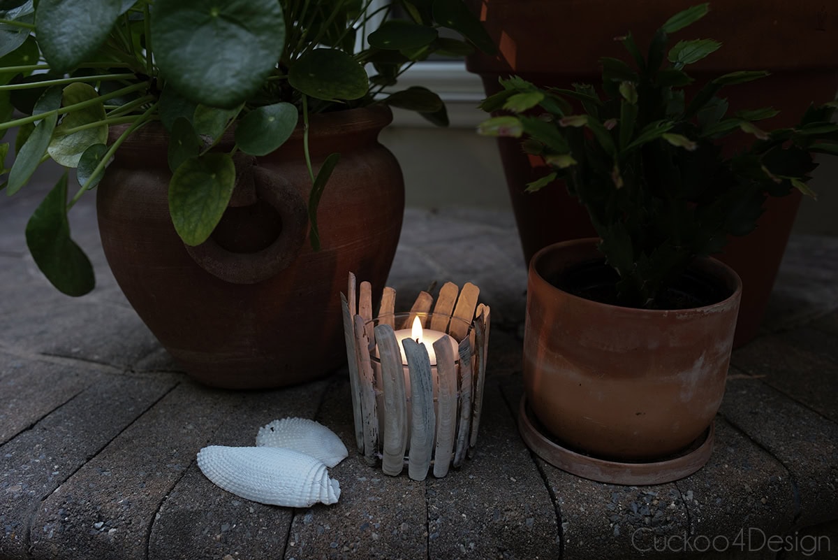 seashell candle holder using razor clamshells on jute yarn, with lit candle in the dark, surrounded by terracotta planters