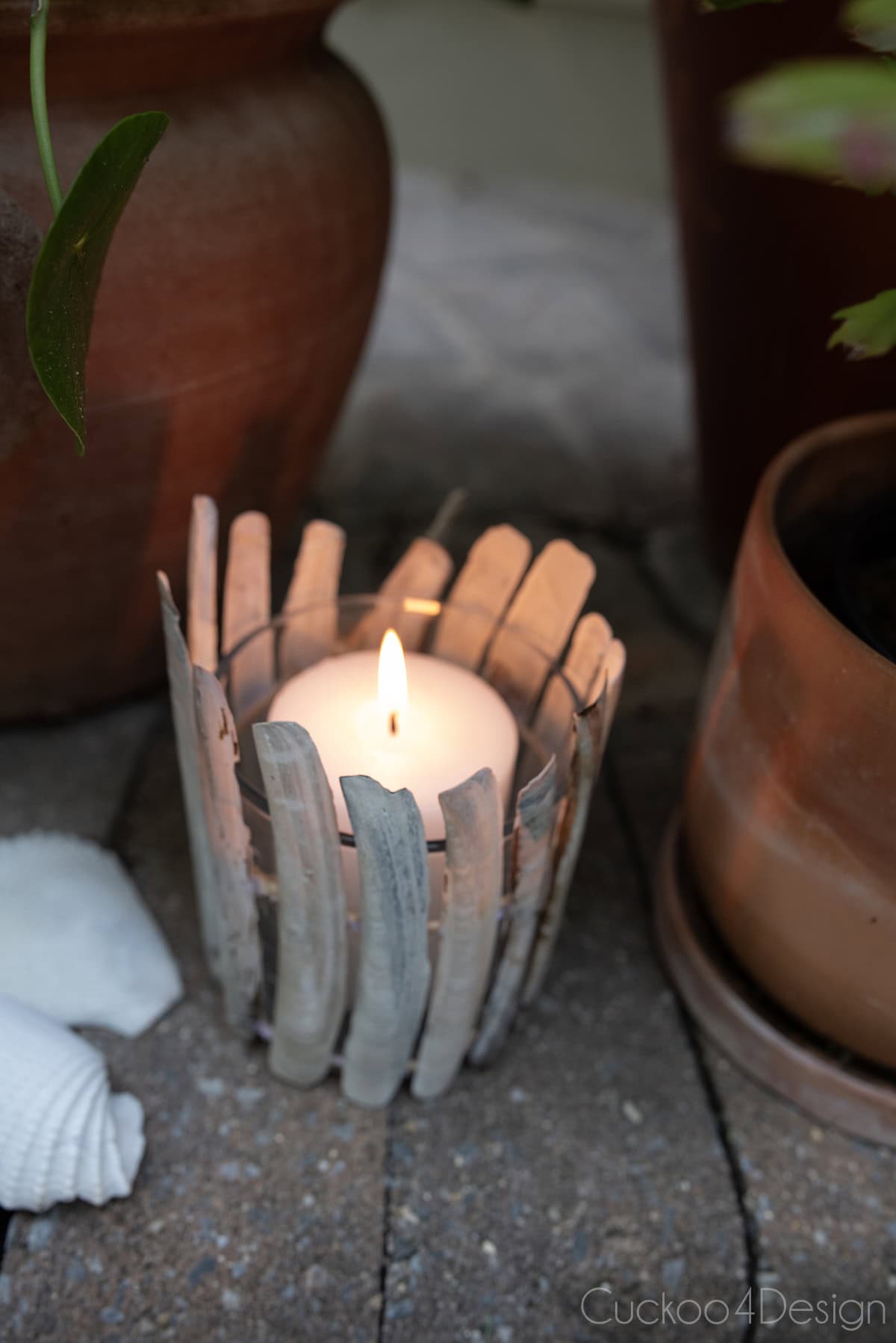 close-up of seashell candle holder using razor clamshells on jute yarn, with lit candle, surrounded by terracotta planters