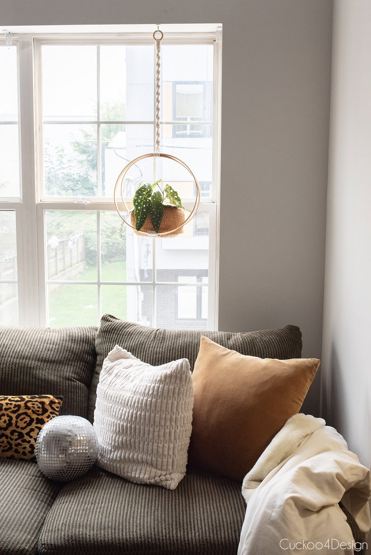 macrame plant hanger made from embroidery hoops hanging above a green corduroy sofa