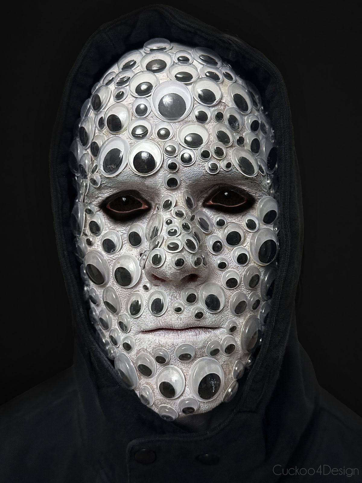 a man wearing black outfit and a full face of googly eyes glued to the face with all black sclera contact lenses