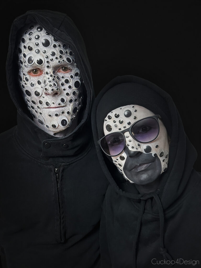 two people wearing black outfits, with one person having a full face of googly eyes glued to the face and the other having half of the face with googly eyes on a black background