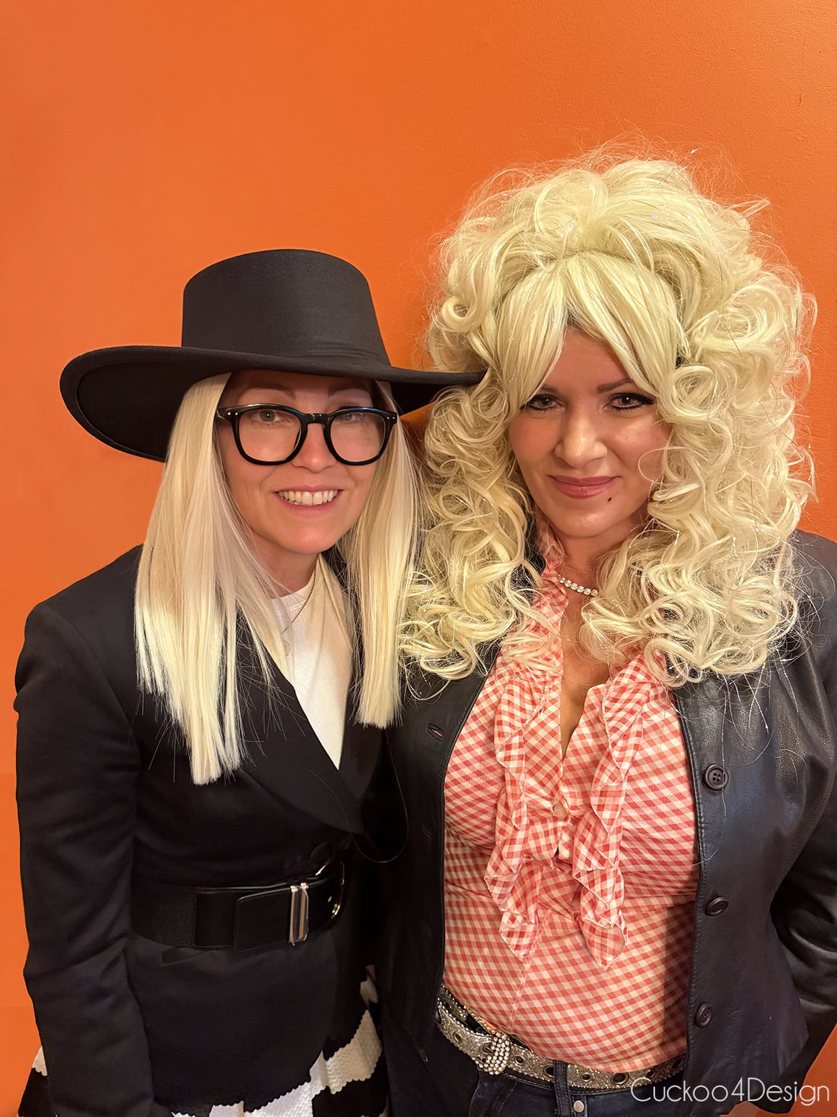 two women at a Halloween party, one in a Diane Keaton costume with a black hat, glasses, and blazer, the other in a big blonde Dolly Parton wig and red ruffled blouse