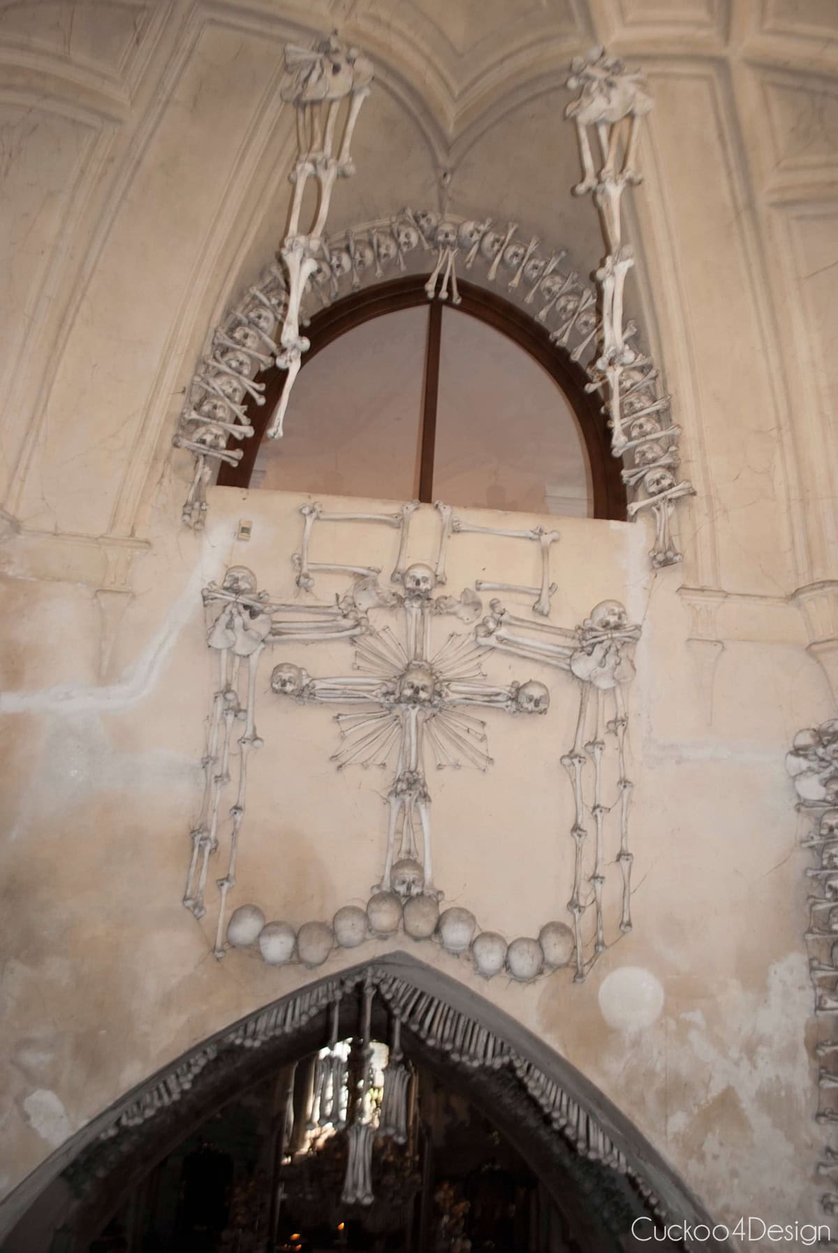 Cross made of bones and skulls with a sunburst of bones above an arch in the Sedlec Ossuary