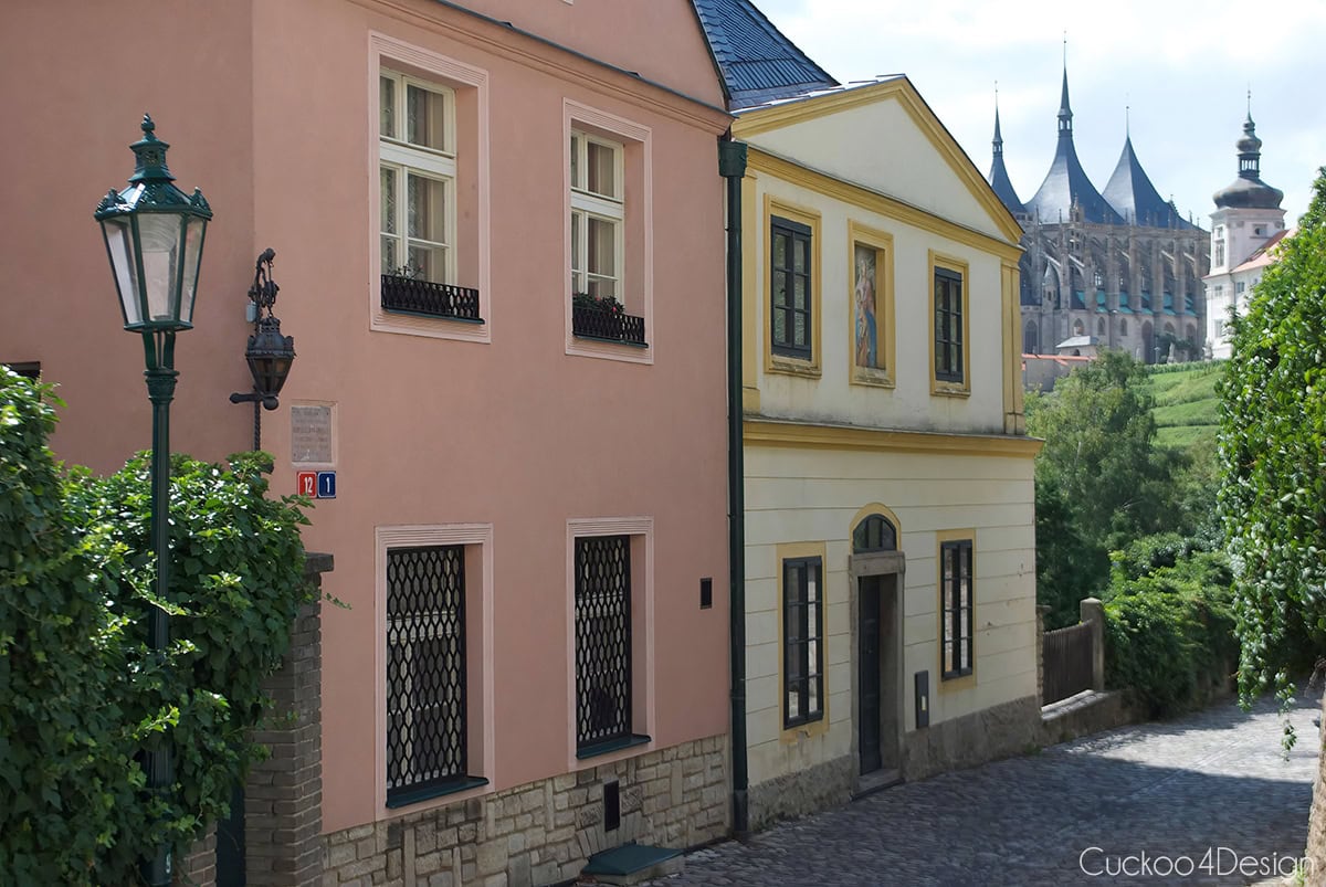 Pink and yellow houses on a cobblestone lane with St. Barbara’s Church in the distance in Kutná Hora