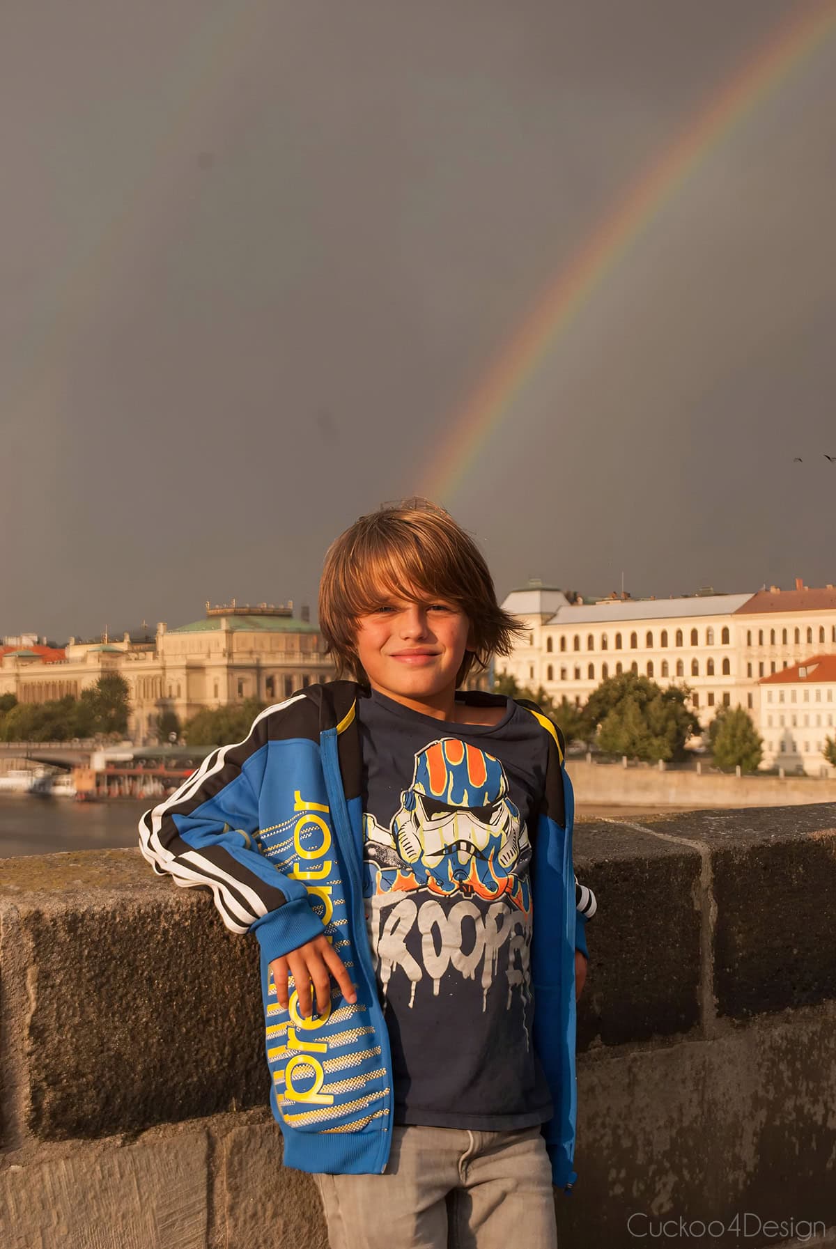 Boy smiling on Charles Bridge in Prague under a rainbow after the rain
