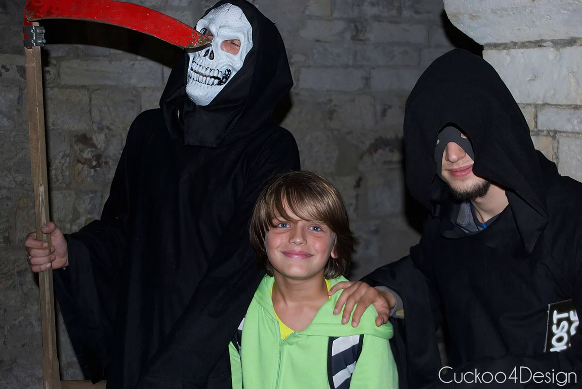 Smiling boy between two hooded guides in costume on a night ghost tour in Prague