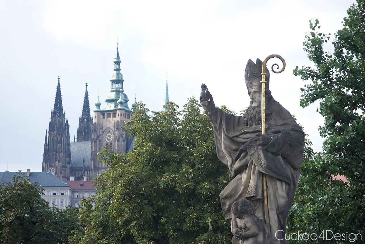 Baroque statue of a bishop on Charles Bridge with St. Vitus Cathedral in the background