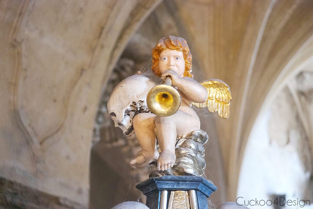 Gilded baroque cherub blowing a trumpet beside a skull inside the Sedlec Ossuary