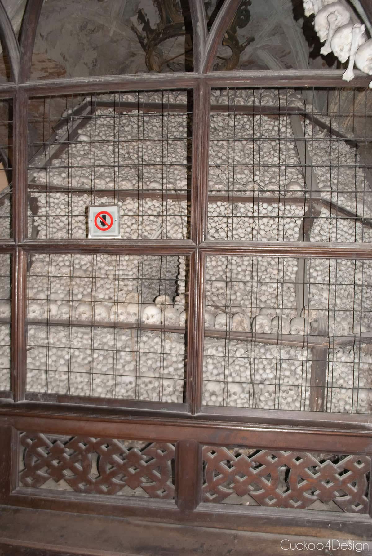 One of the bone pyramids in the Sedlec Ossuary, made of stacked skulls and bones behind a wooden frame and wire grate