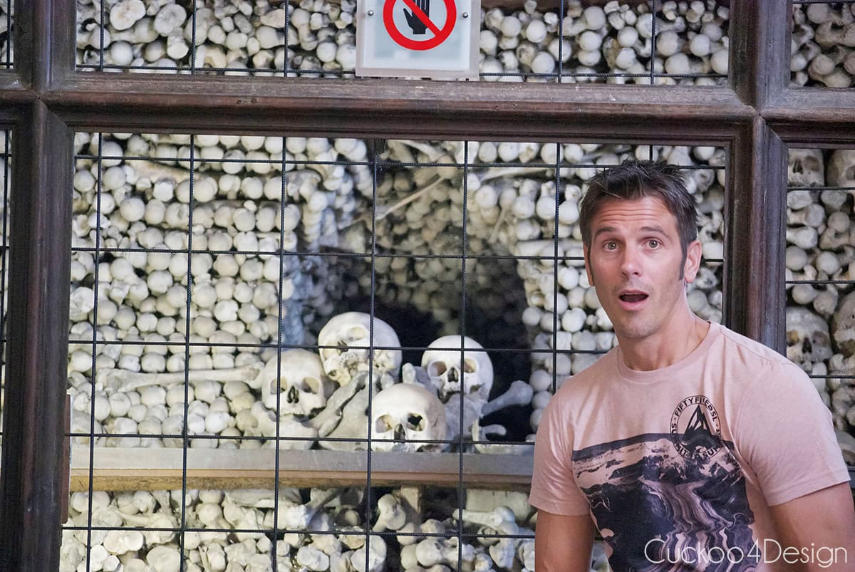 Visitor with a surprised expression standing in front of a bone pyramid at the Sedlec Ossuary