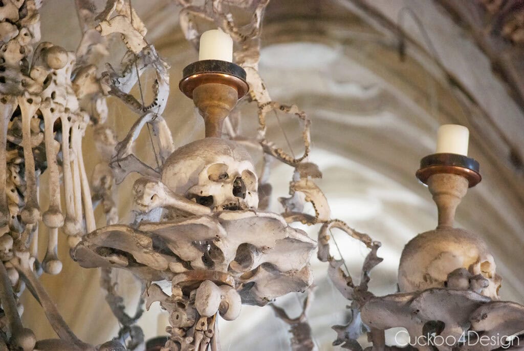 Close-up of the Sedlec Ossuary bone chandelier, with a candle on a skull and crossbones, pelvis bones, and garlands of jawbones