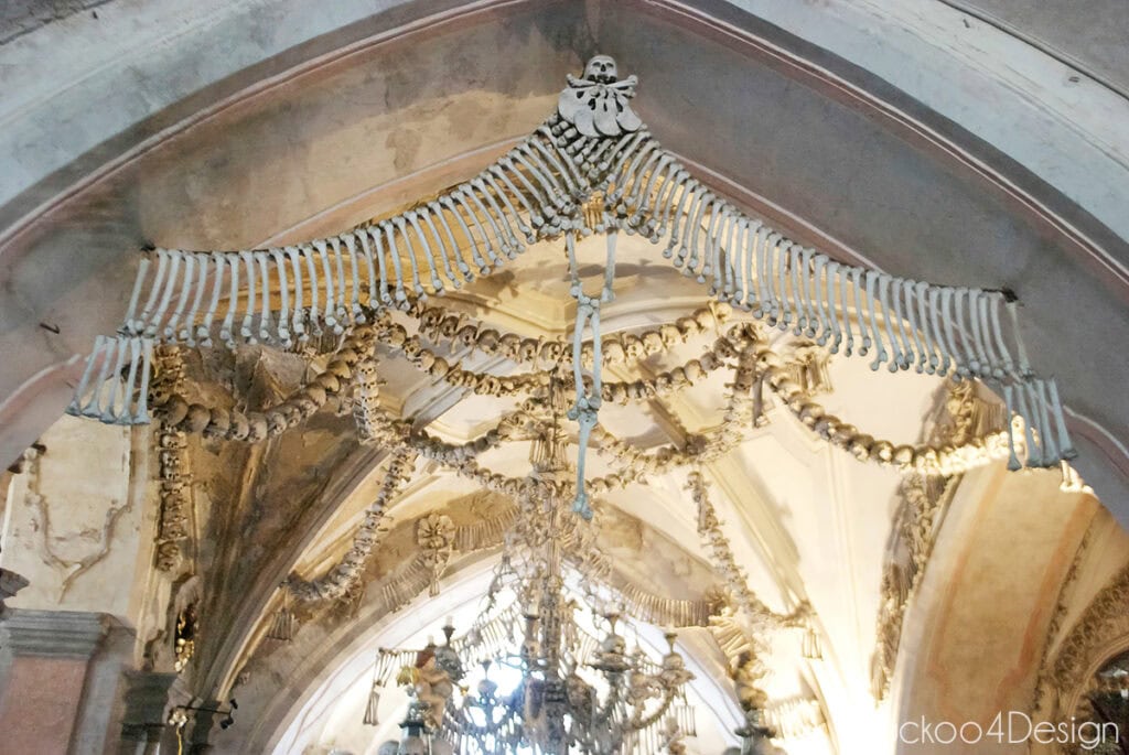 Garlands of skulls and a fringe of bones hanging from the vaulted ceiling of the Sedlec Ossuary, with the bone chandelier below